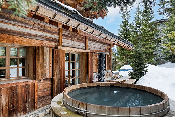 A wooden hot tub sits outside of a wooden cabin