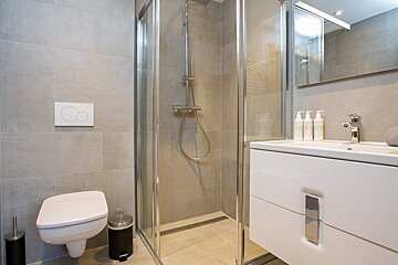 Modern bathroom with grey tiles, a glass shower enclosure, a wall-mounted toilet, and a white sink vanity.
