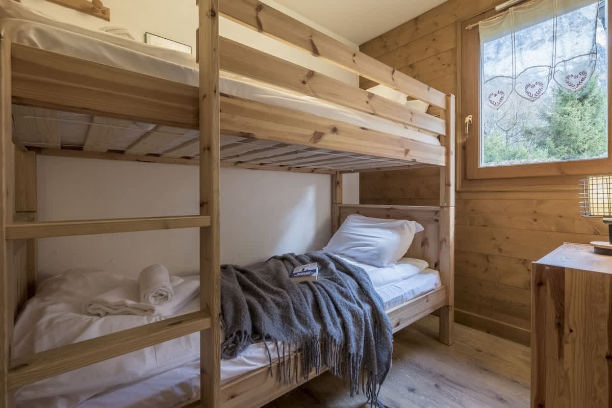 A cozy rustic bedroom featuring wooden bunk beds, wood-paneled walls, and a window looking outside.