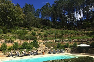 A swimming pool surrounded by chairs and trees on a hillside