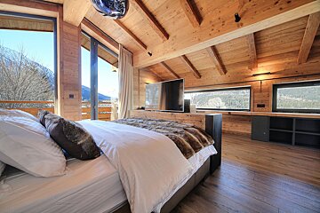 Luxurious alpine-style bedroom with a large bed, fur throw, and TV, featuring floor-to-ceiling windows with a stunning snowy mountain view.