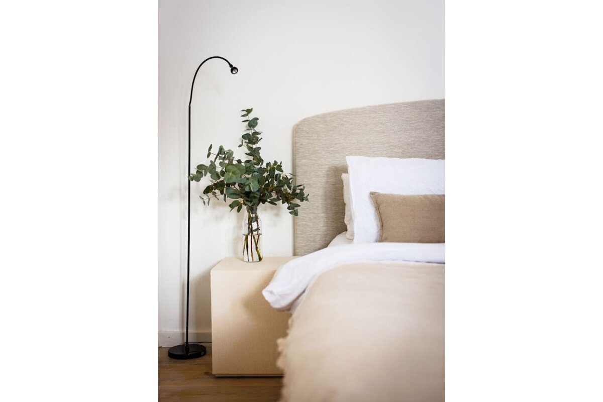 A vase of flowers sits on a nightstand next to a bed