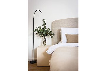 A vase of flowers sits on a nightstand next to a bed