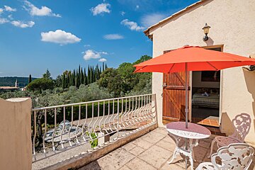 A balcony with a table and chairs and an orange umbrella