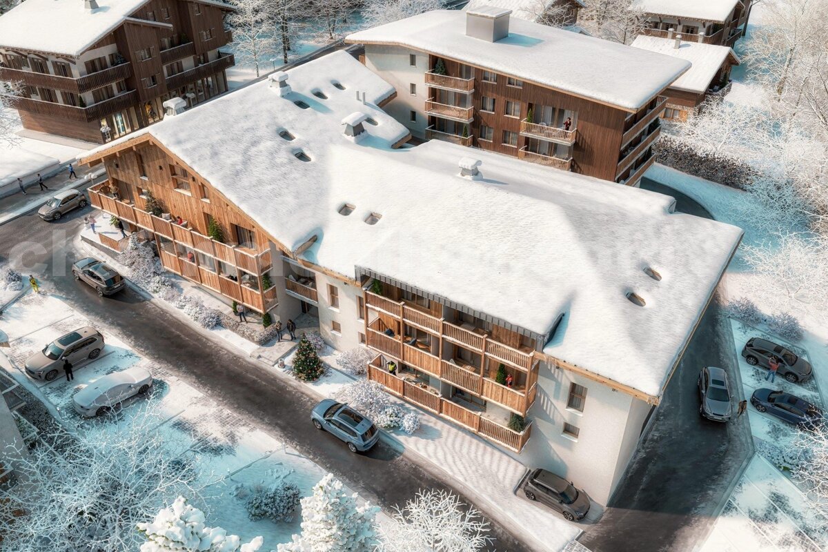 Aerial shot of snow-covered chalet-style apartment buildings with balconies, cars, and frosted trees in a serene winter landscape.
