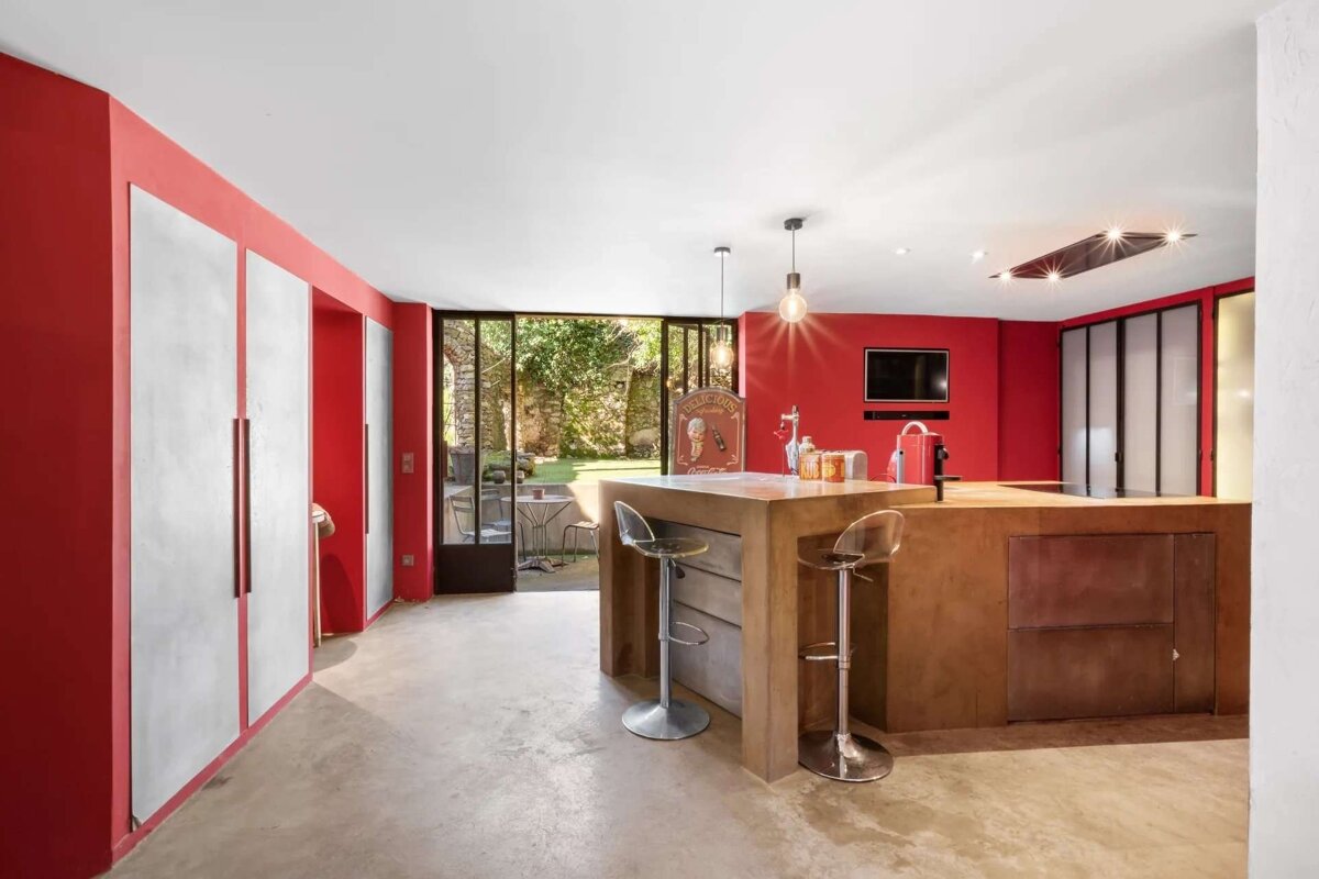 Modern kitchen with bold red walls, concrete bar island, concrete floor, and glass doors leading to a garden.