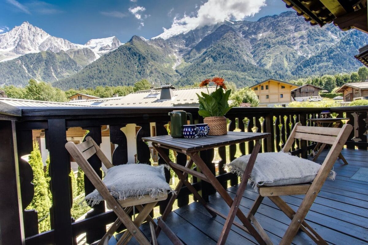 A balcony with a table and chairs and mountains in the background