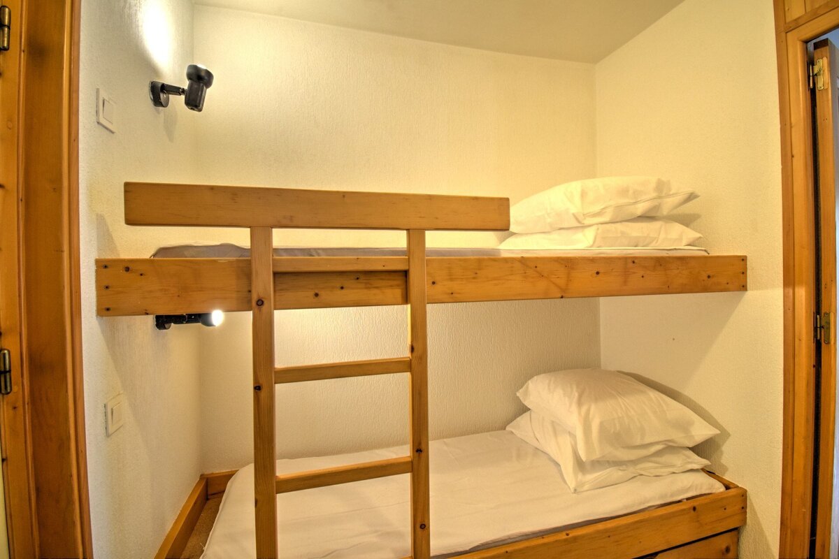 A cozy room featuring wooden bunk beds with white bedding, individual reading lights, and a ladder for the top bunk.