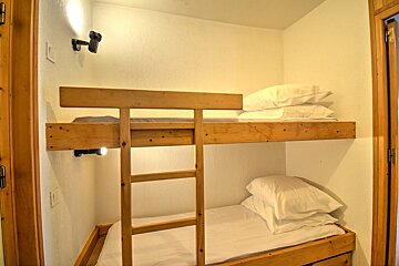 Simple wooden bunk beds with white sheets and pillows tucked into a cozy, narrow room.
