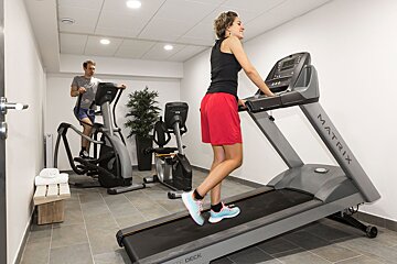 A woman is running on a matrix treadmill in a gym