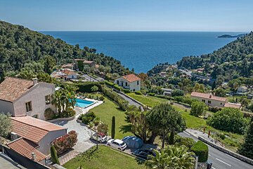 Scenic view of coastal villas with a pool on a lush green hillside overlooking the deep blue sea.