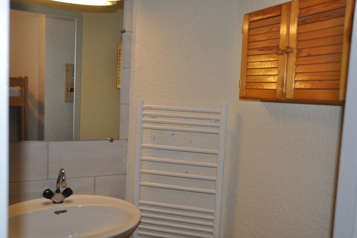 A small bathroom featuring a sink, mirror reflecting bunk beds, a white towel radiator, and a wooden slatted wall cabinet.
