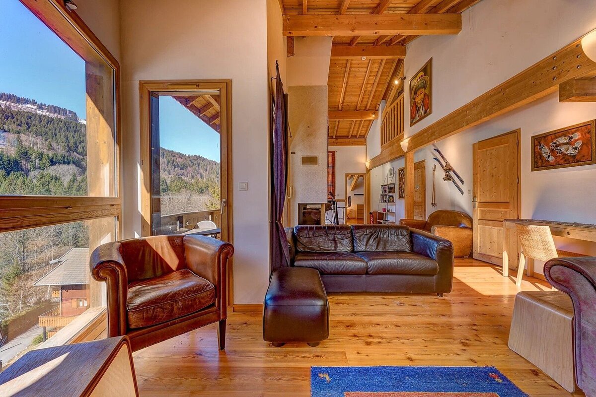 Cozy alpine cabin interior with wooden beams, leather furniture, and a large window showcasing beautiful mountain views.
