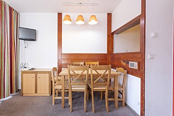 A rustic dining space featuring a wooden table and chairs, wall-mounted TV, wood paneling, and colorful striped curtains.