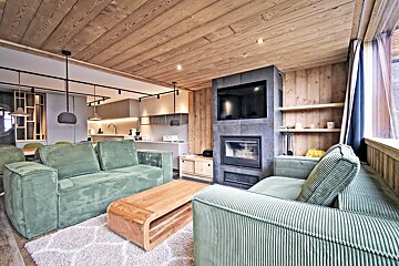 Modern chalet living room featuring wood paneling, green corduroy sofas, a wooden coffee table, and a built-in fireplace.