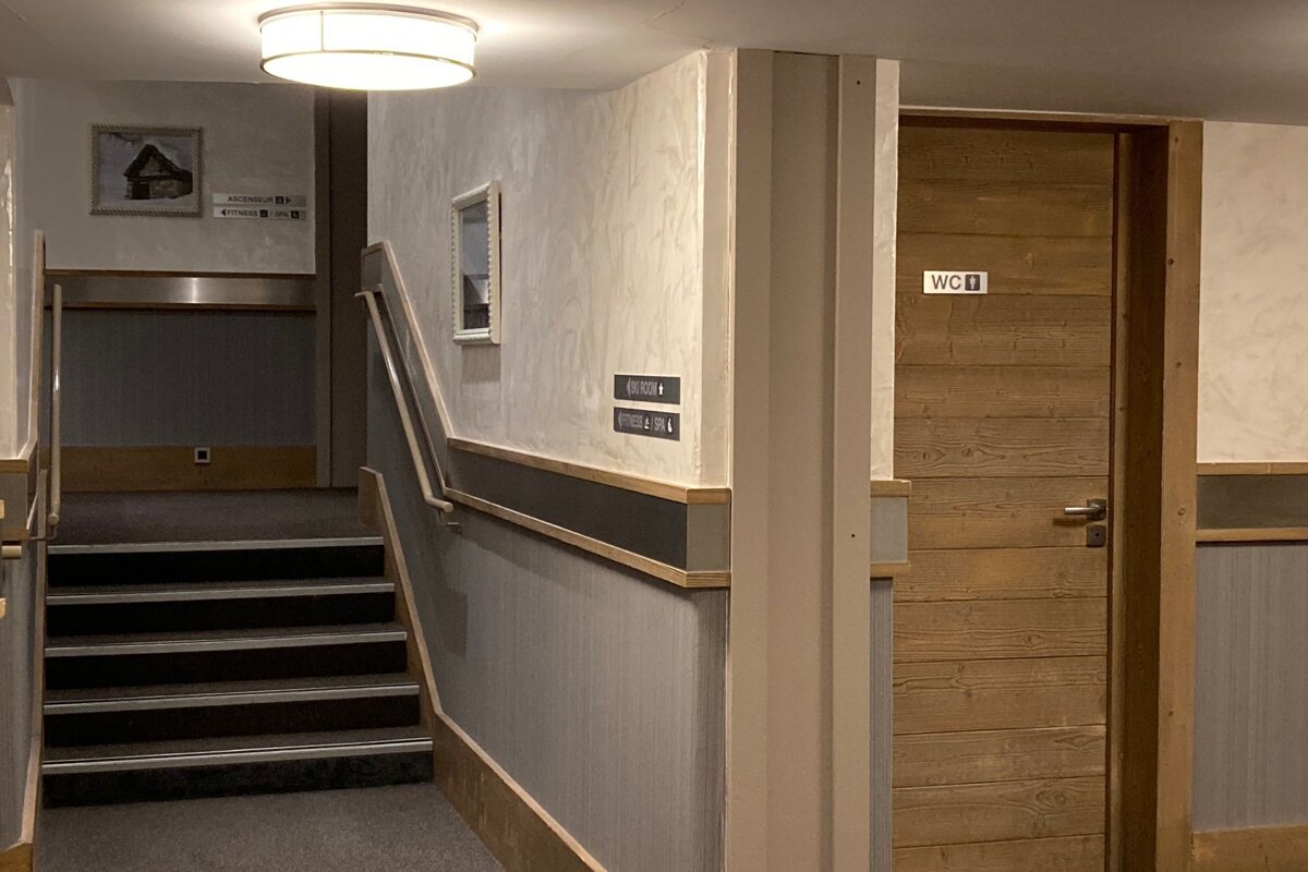 A hotel hallway featuring carpeted stairs on the left and a wooden restroom door labeled "WC" on the right.