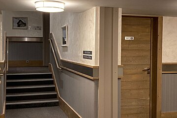 A hotel hallway featuring carpeted stairs on the left and a wooden restroom door labeled "WC" on the right.
