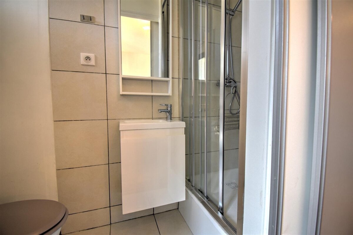 A compact, tiled bathroom featuring a floating white vanity sink, a mirror, and a glass-door shower.