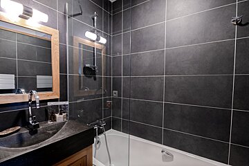 A bathroom with black tiles and a bathtub