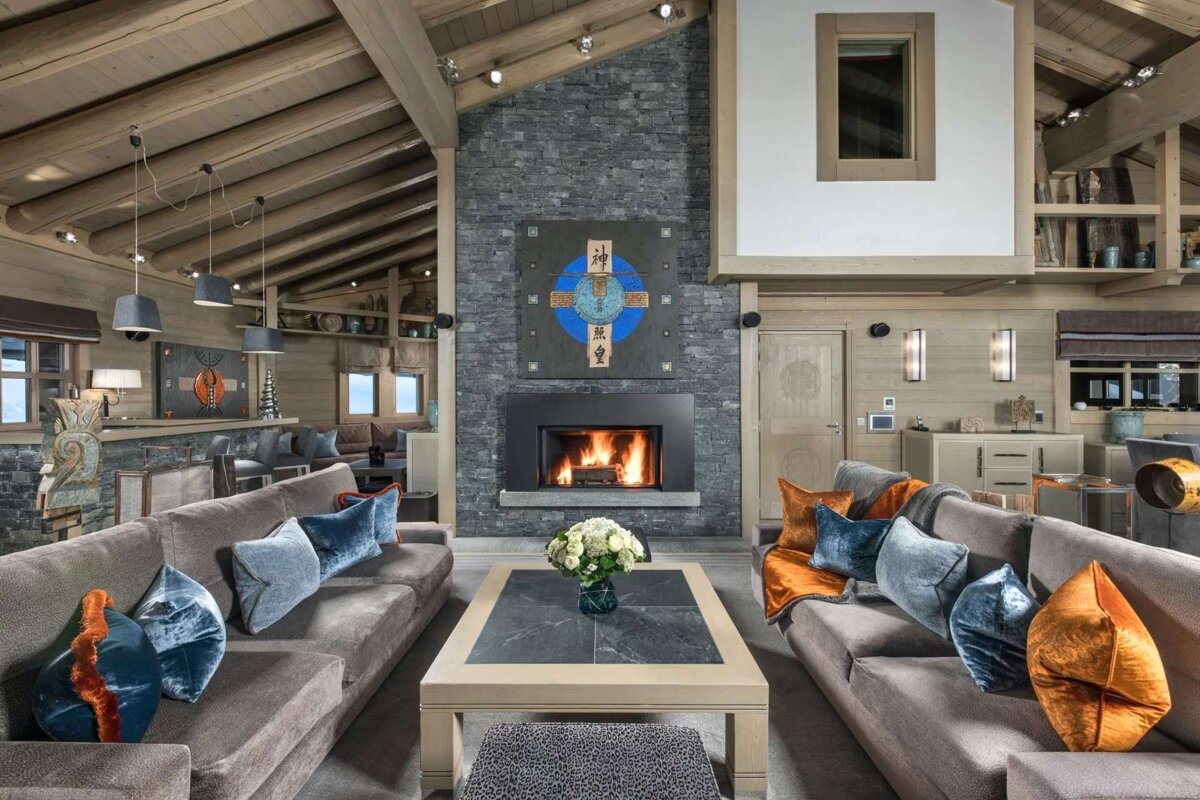 A luxurious, spacious chalet living room with a grand stone fireplace, high wood ceilings, and cozy sofas adorned with vibrant pillows.