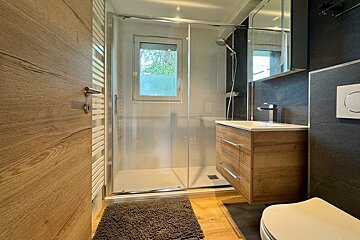 Modern bathroom featuring a glass-enclosed shower, a floating wooden vanity, and a matching wooden door.