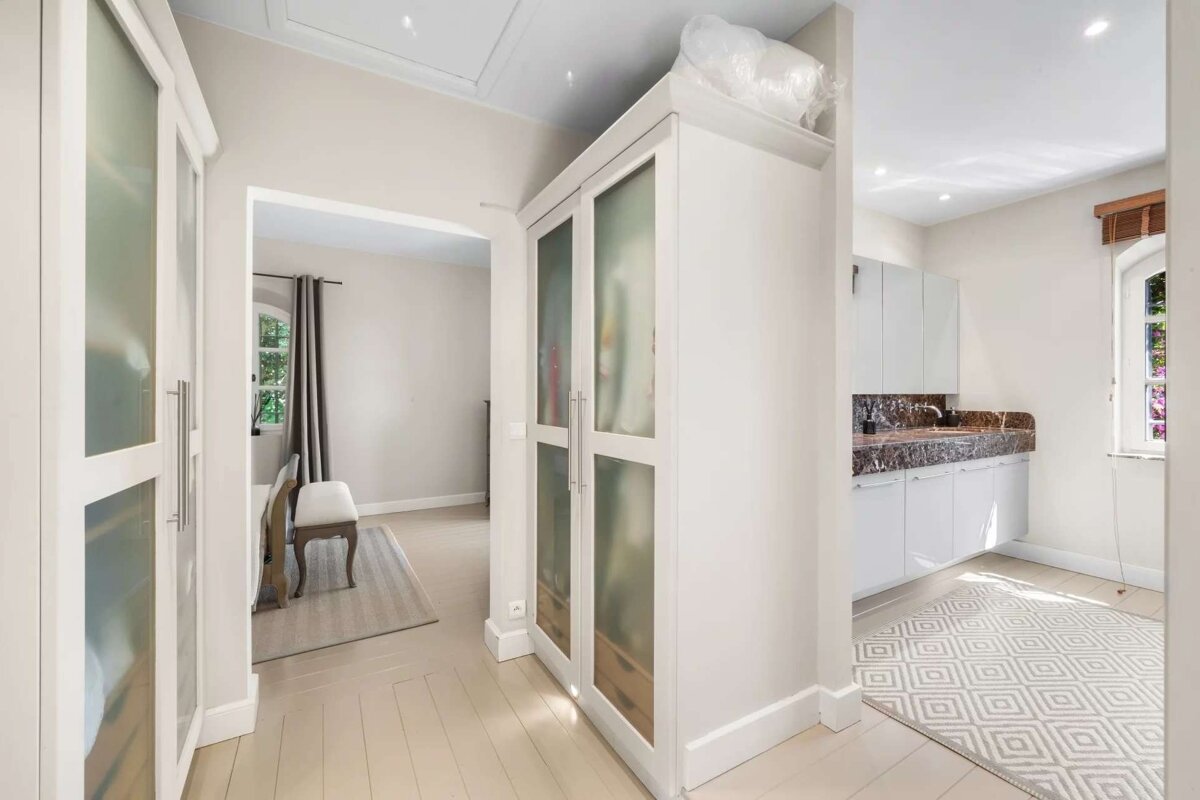 Bright, modern interior featuring a white frosted-glass cabinet dividing a dining area from a kitchen/utility space with white cabinets and a patterned rug.