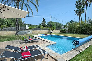 A large swimming pool is surrounded by lawn chairs and a white umbrella