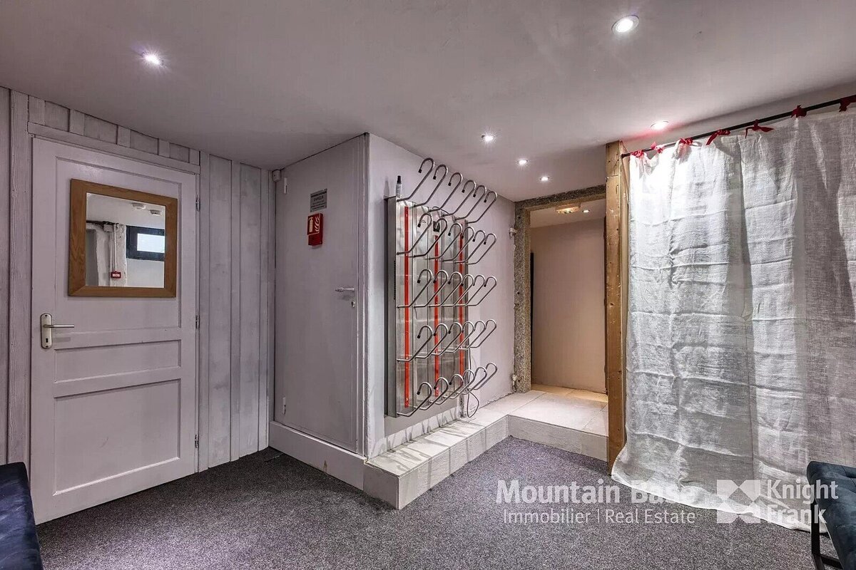 A practical entryway with a large boot drying rack, a white door with a mirror, and a light curtain covering an alcove, on grey carpet.
