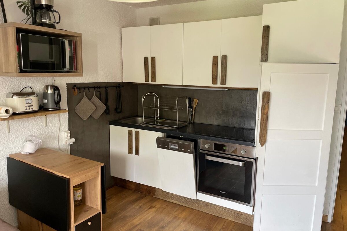 A cozy kitchen featuring white cabinets, unique wooden handles, microwave, coffee maker, sink, dishwasher, oven, and a folding table.