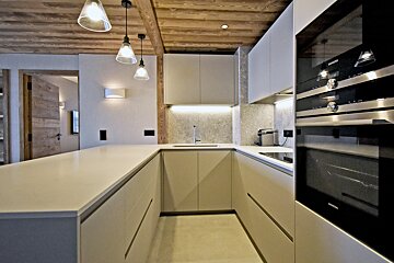 A contemporary U-shaped kitchen with light beige cabinets, built-in ovens, elegant pendant lights, and a rustic wooden ceiling.