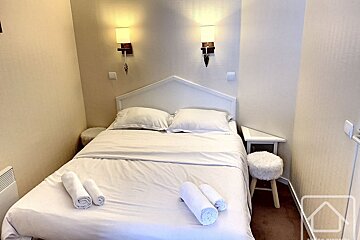 A bed with white sheets and pillows in a small room