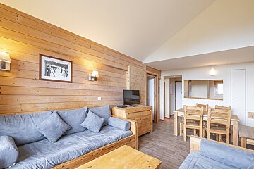 A cozy, rustic living and dining area with wood paneling, a grey sofa, wooden coffee table, TV, and a wooden dining set.