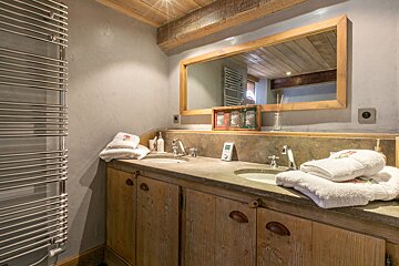 Rustic cabin bathroom featuring a double wooden vanity, stone countertop, large mirror, and a chrome towel warmer.