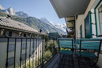 A balcony with chairs and a table with mountains in the background