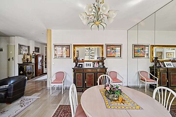 A richly decorated dining room with a large oval table, ornate sideboards, framed art, a chandelier, and a mirrored wall reflecting the space.