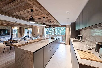 A luxurious, modern kitchen and dining area features wooden beamed ceilings, marble countertops, an island, and large windows looking out to nature.