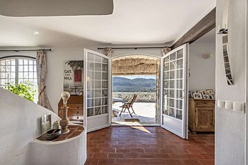 Bright, rustic room with terracotta floor. French doors open to a sunny patio overlooking mountains. Warm Mediterranean style interior.