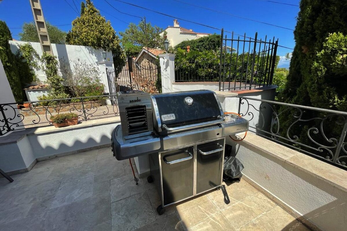 A weber grill sits on a patio next to a fence