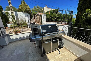 A weber grill sits on a patio next to a fence