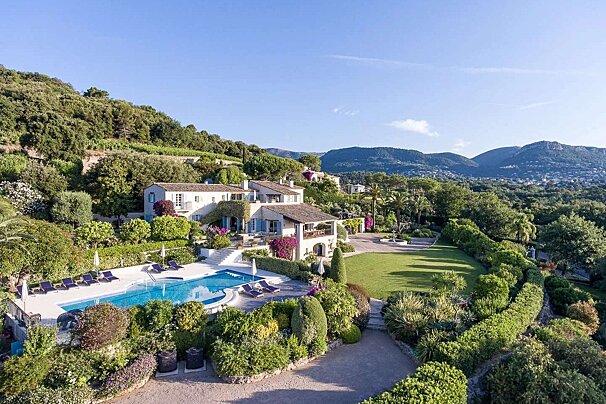 A large house sits on top of a hill with mountains in the background