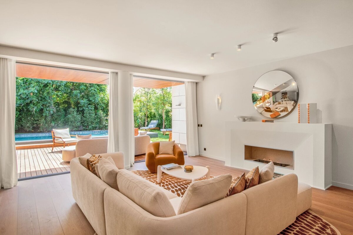 Bright, modern living room with a large sofa, fireplace, and sliding doors opening to an outdoor deck and swimming pool.
