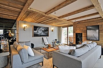 Rustic-modern living room with wooden ceilings & walls, grey sofas, a fireplace, and large windows opening to a balcony.