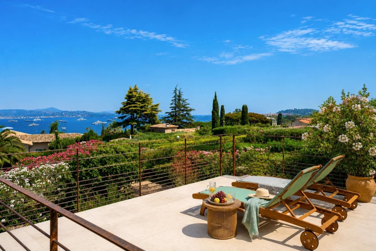 Sunny villa terrace with wooden loungers overlooking a lush garden and the blue Mediterranean Sea.