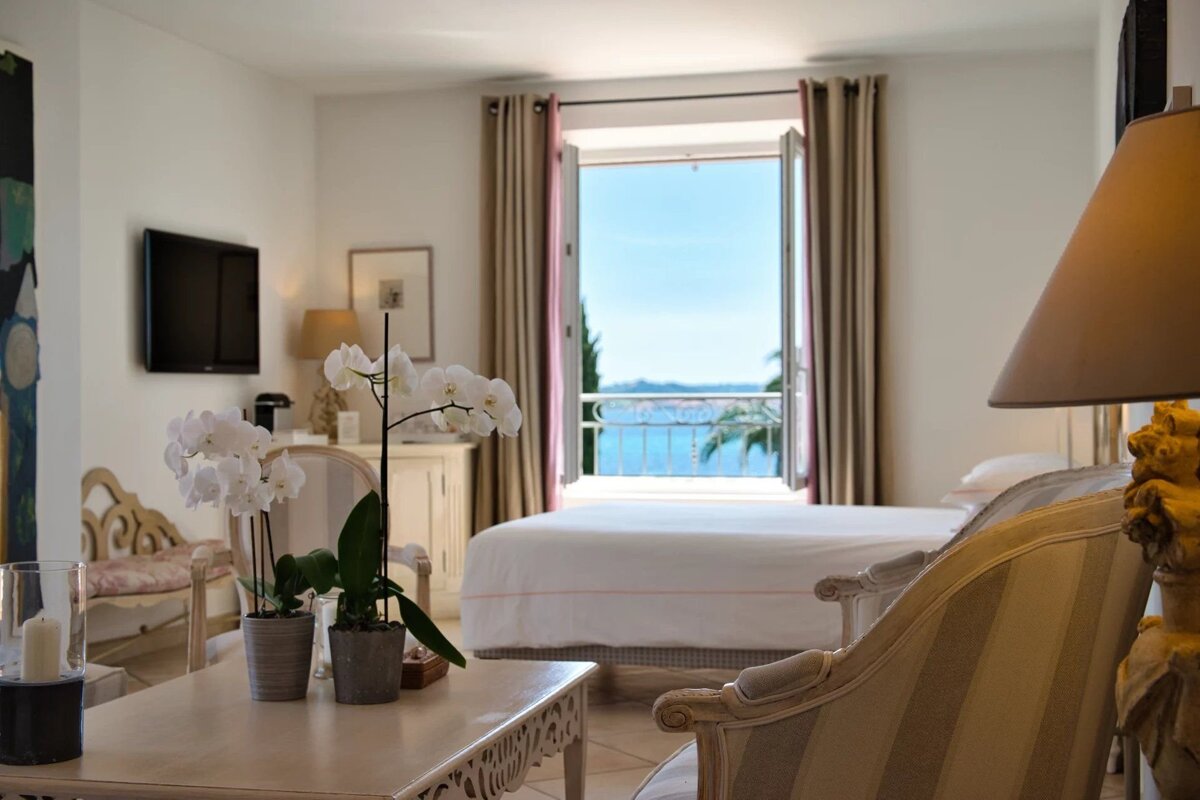 Bright room with white orchids and elegant decor. Open doors reveal a beautiful blue sea view and coastline.