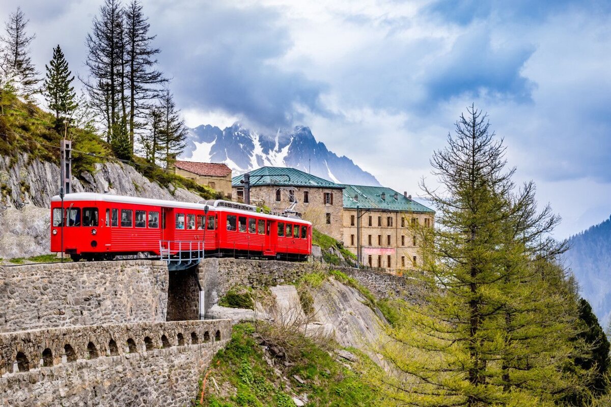 A red train is going down a hill with mountains in the background