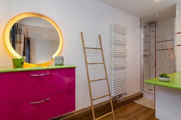 A bathroom with pink cabinets and a round mirror