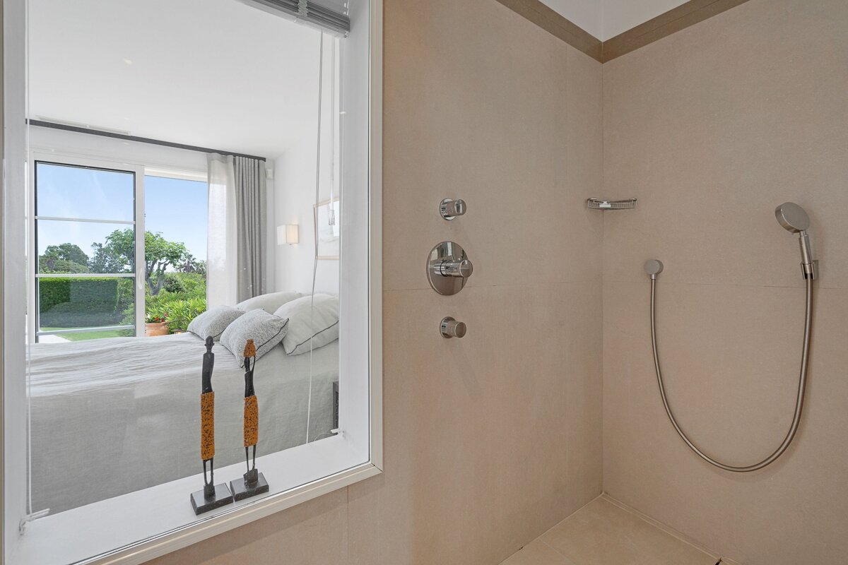 A bathroom with a shower and a window with a view of a bedroom