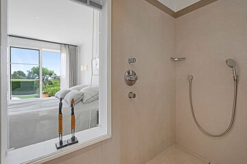 A bathroom with a shower and a window with a view of a bedroom