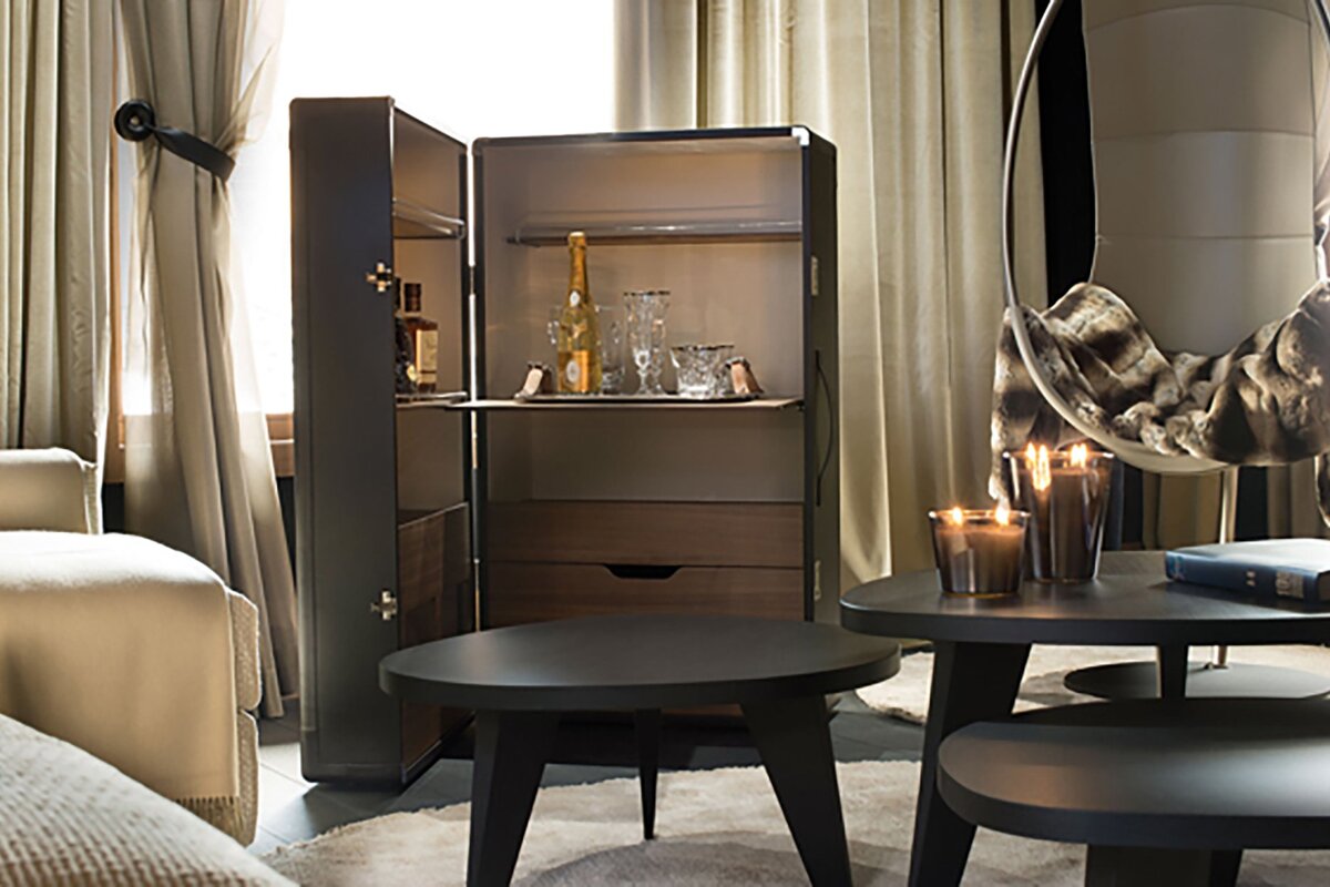 An elegant living room features an open bar cabinet with drinks and glasses, dark coffee tables with candles, and a hanging chair.