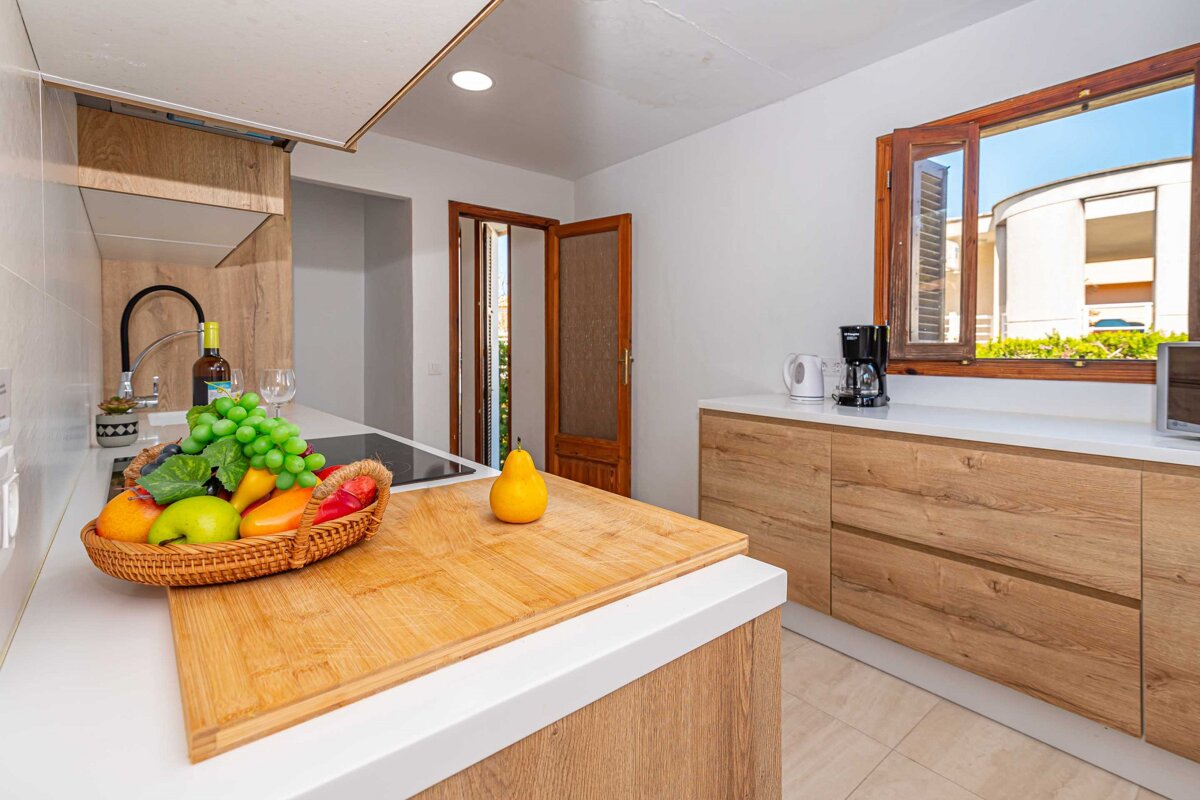 A basket of fruit sits on a cutting board in a kitchen